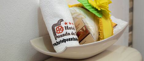 A white towel with a hotel logo and website URL, a yellow flower, and a chocolate bar in a white bowl.