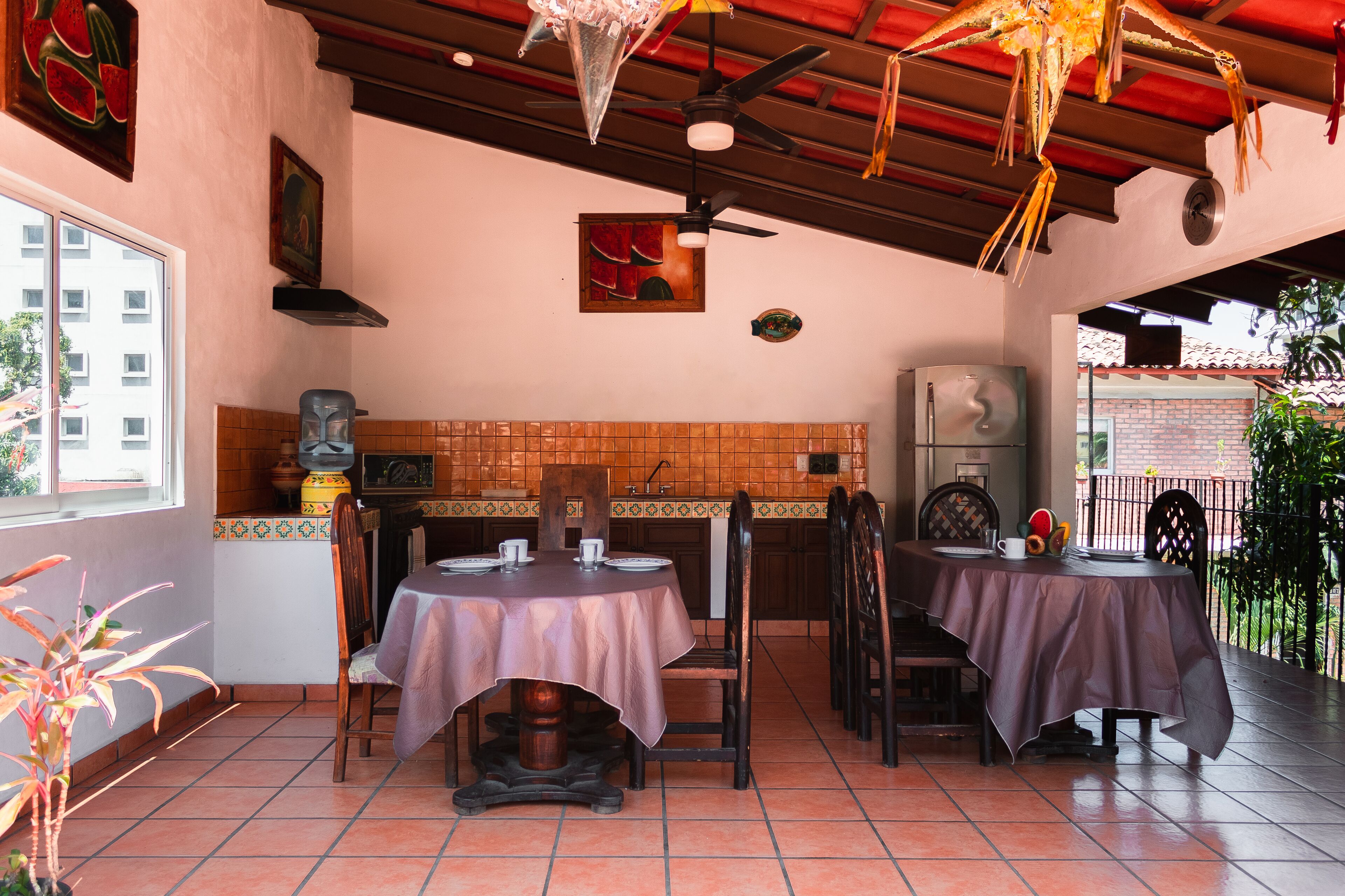 Un restaurant avec deux tables, des chaises, un ventilateur de plafond, des murs carrelés et une vue sur un bâtiment à l’extérieur.