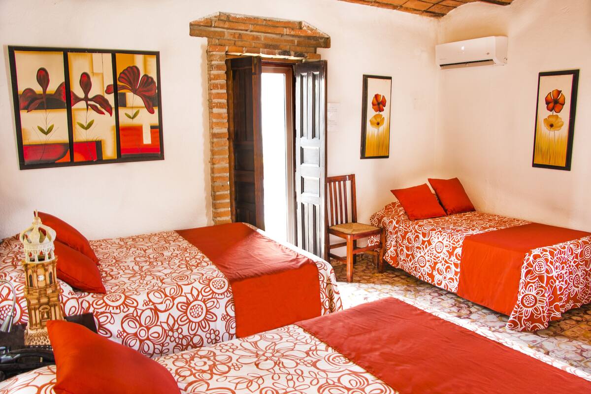 A room with two beds, each with red and white patterned bedding, a wooden chair, and a small table with a decorative item.