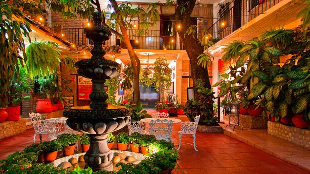 A hotel atrium with a central fountain surrounded by potted plants and white chairs.