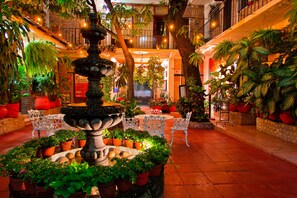 Un vestíbulo de hotel con una fuente central rodeada de plantas en macetas y sillas blancas.