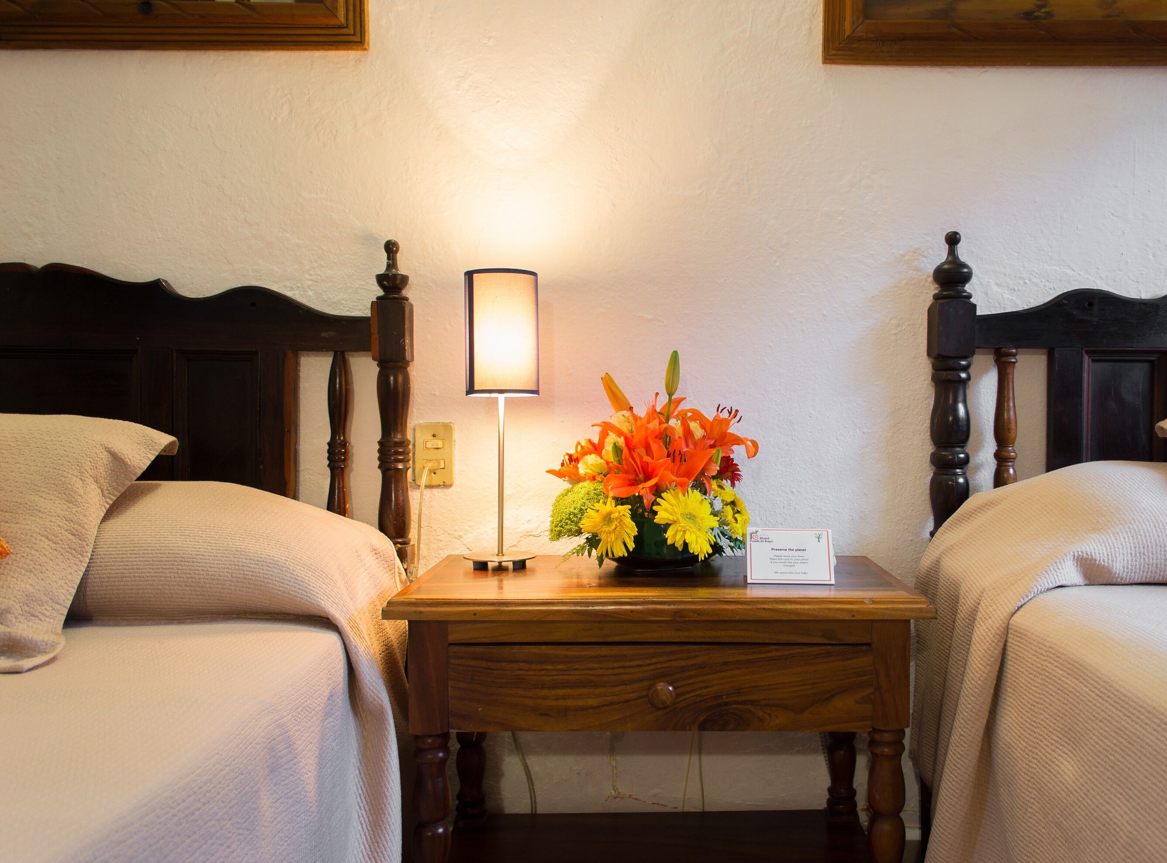 Una habitación de hotel con dos camas, una mesita de noche con lámpara y un arreglo floral.