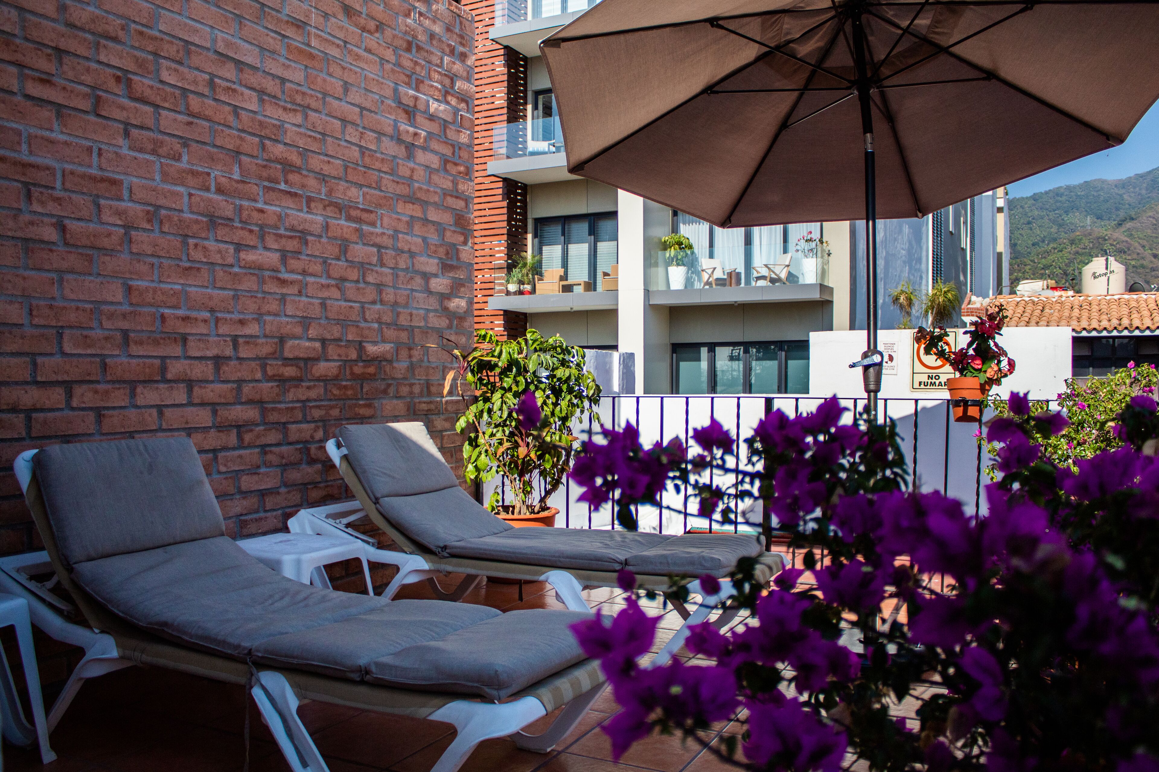 Een balkon met twee loungestoelen, een potplant en een grote parasol.