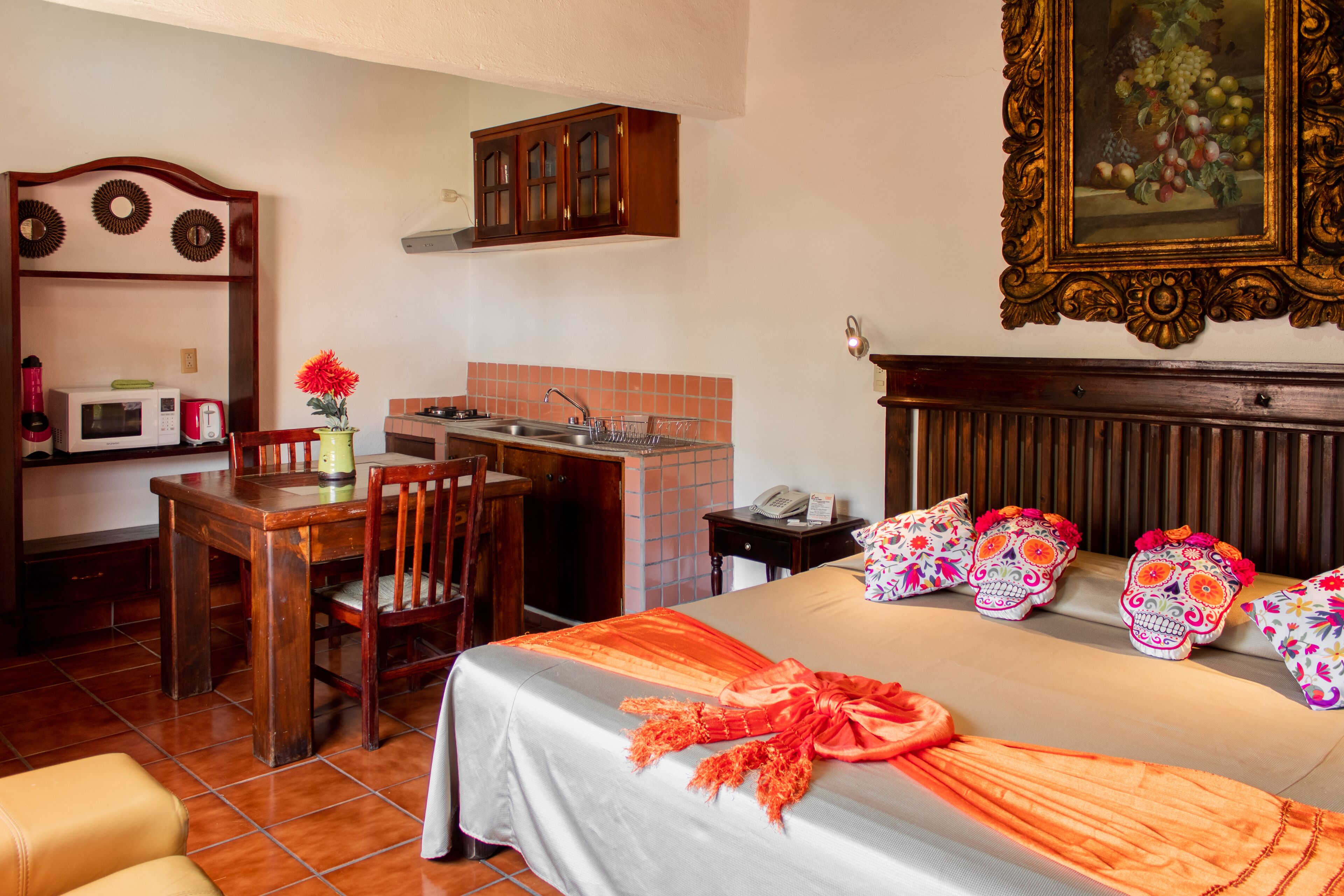 A compact hotel room with a bed, a small desk, a chair, a microwave, a sink, and a cabinet.