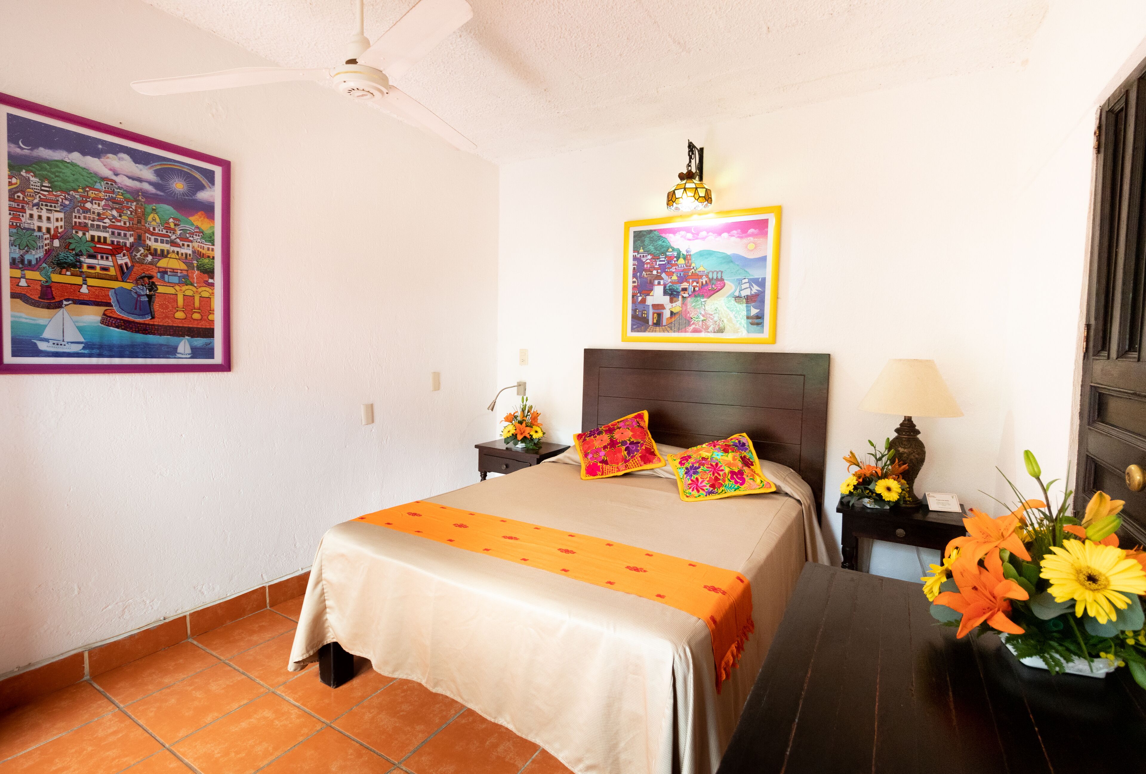 Una habitación de hotel con una cama, una mesita de noche, una lámpara y un jarrón de flores.