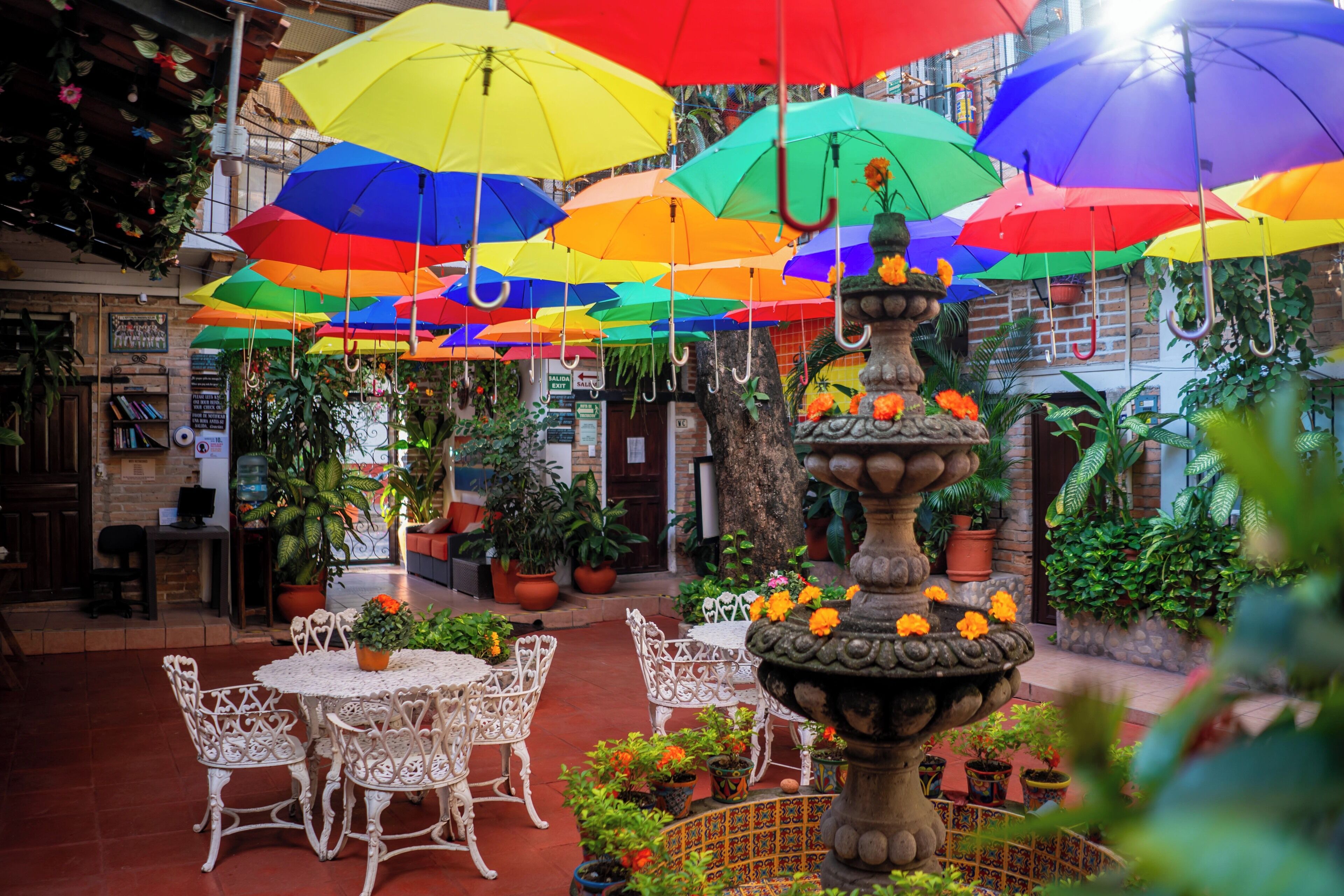 Un patio con mobiliario blanco para exteriores, una fuente central y sombrillas de colores.