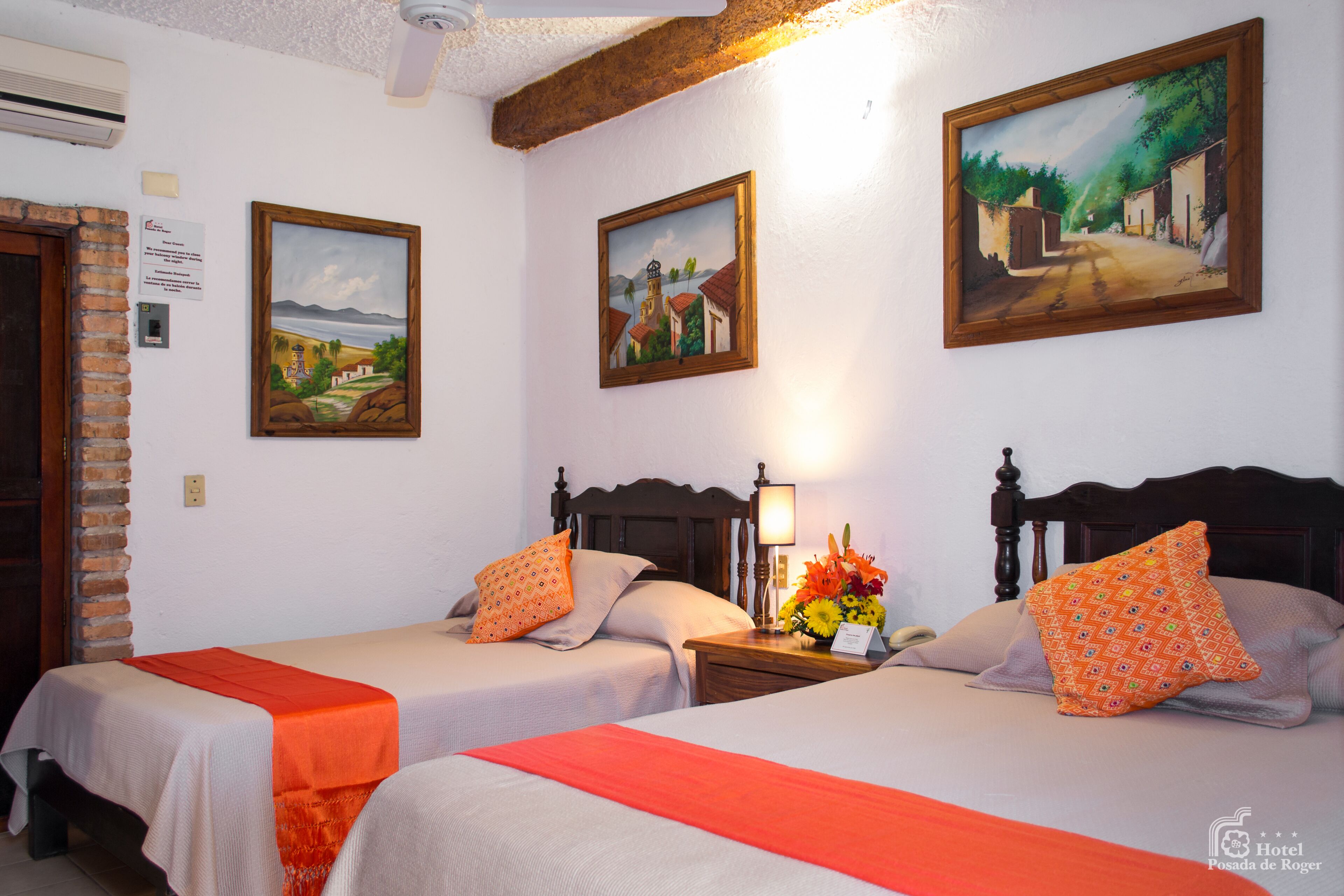 A hotel room with two beds, a brick wall, and three paintings on the wall.