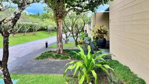 A pathway leading to a building with a modern design, surrounded by greenery and potted plants.