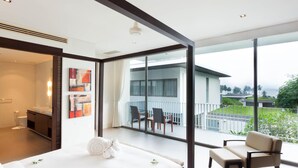 A modern hotel room with a large bed, a balcony with chairs, and a view of the sea.