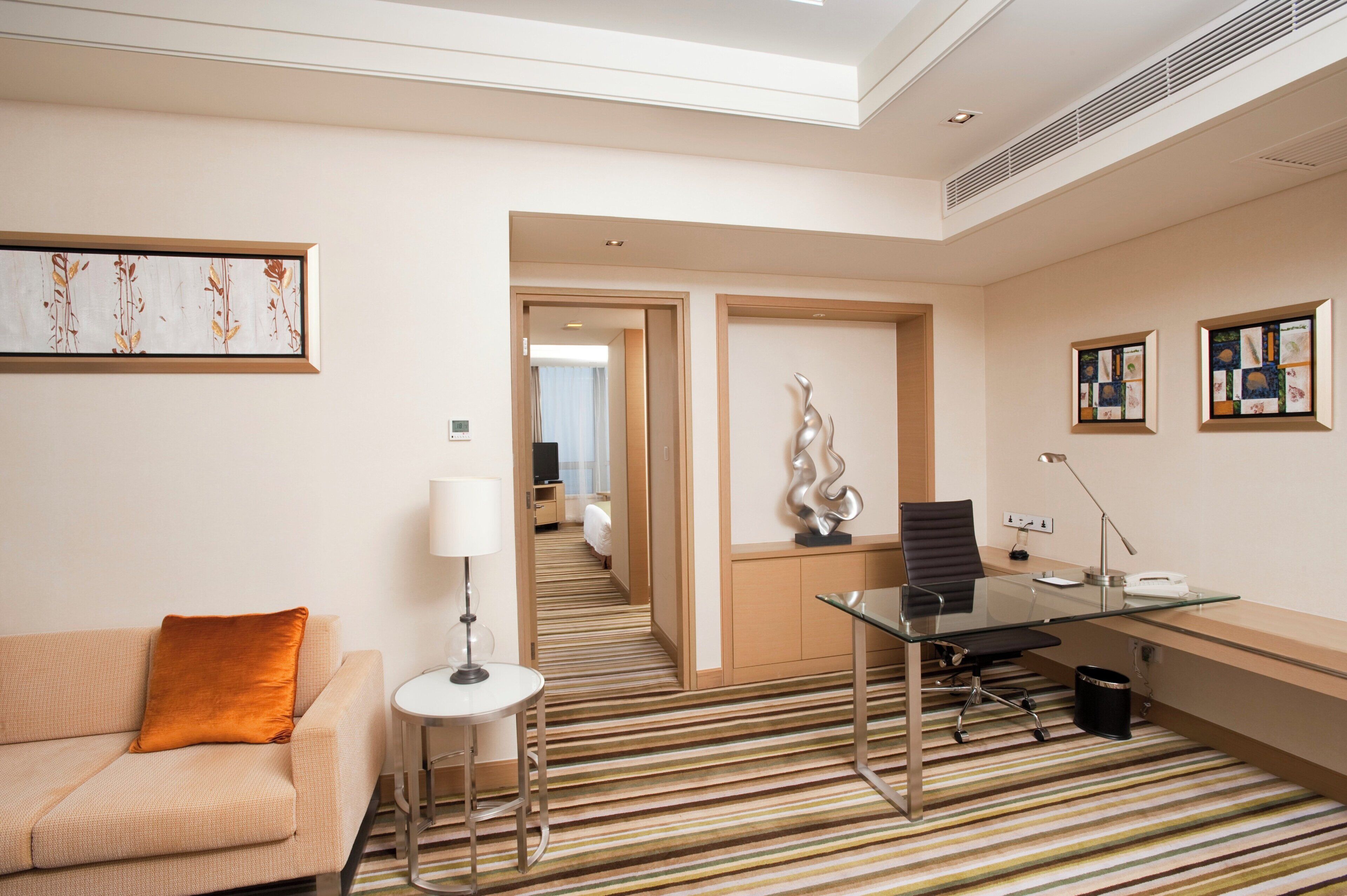 A hotel room with a sofa, a desk with a chair, a lamp, and artwork on the walls.