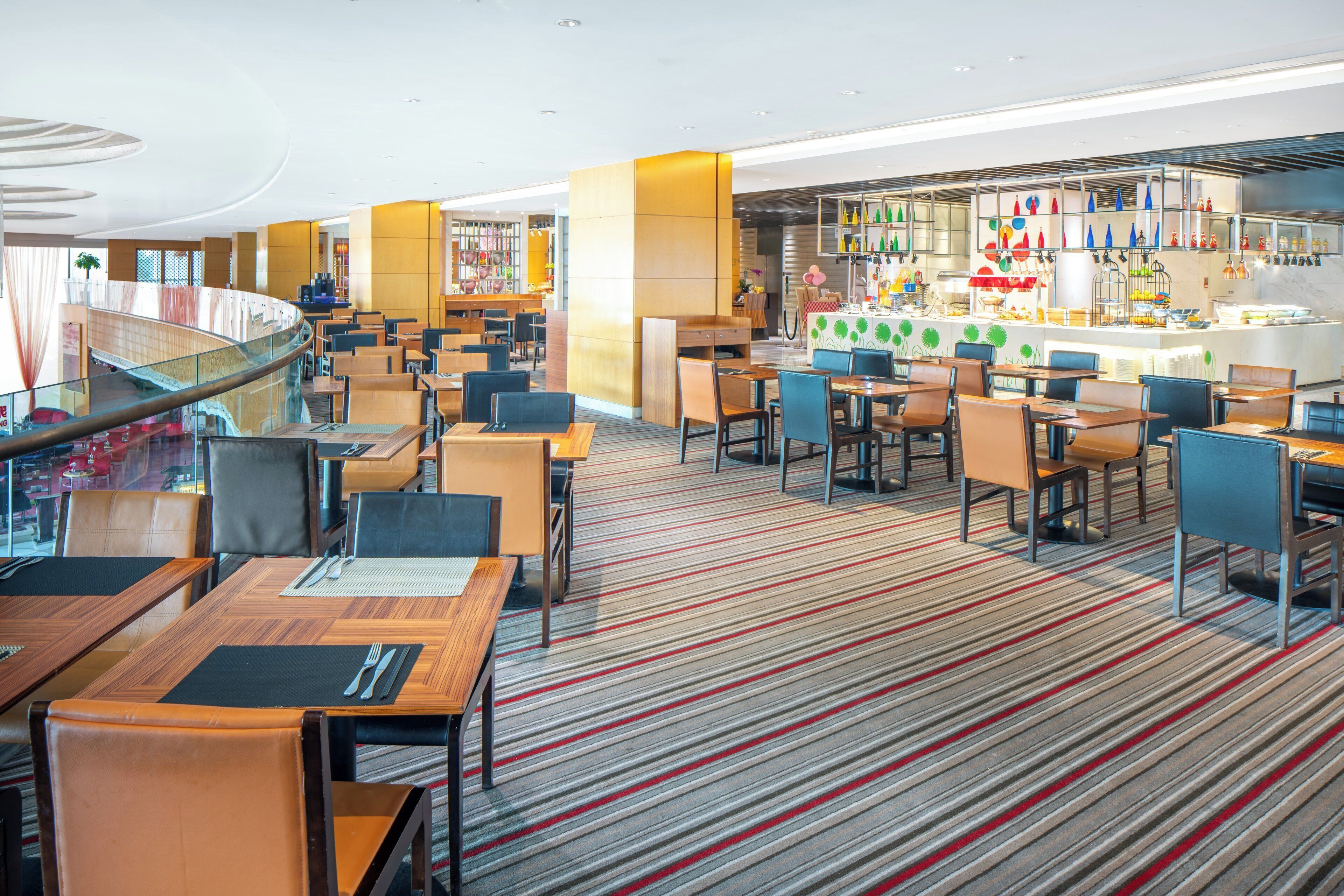 A modern hotel lobby with multiple seating areas, a central bar, and a staircase leading to an upper level.