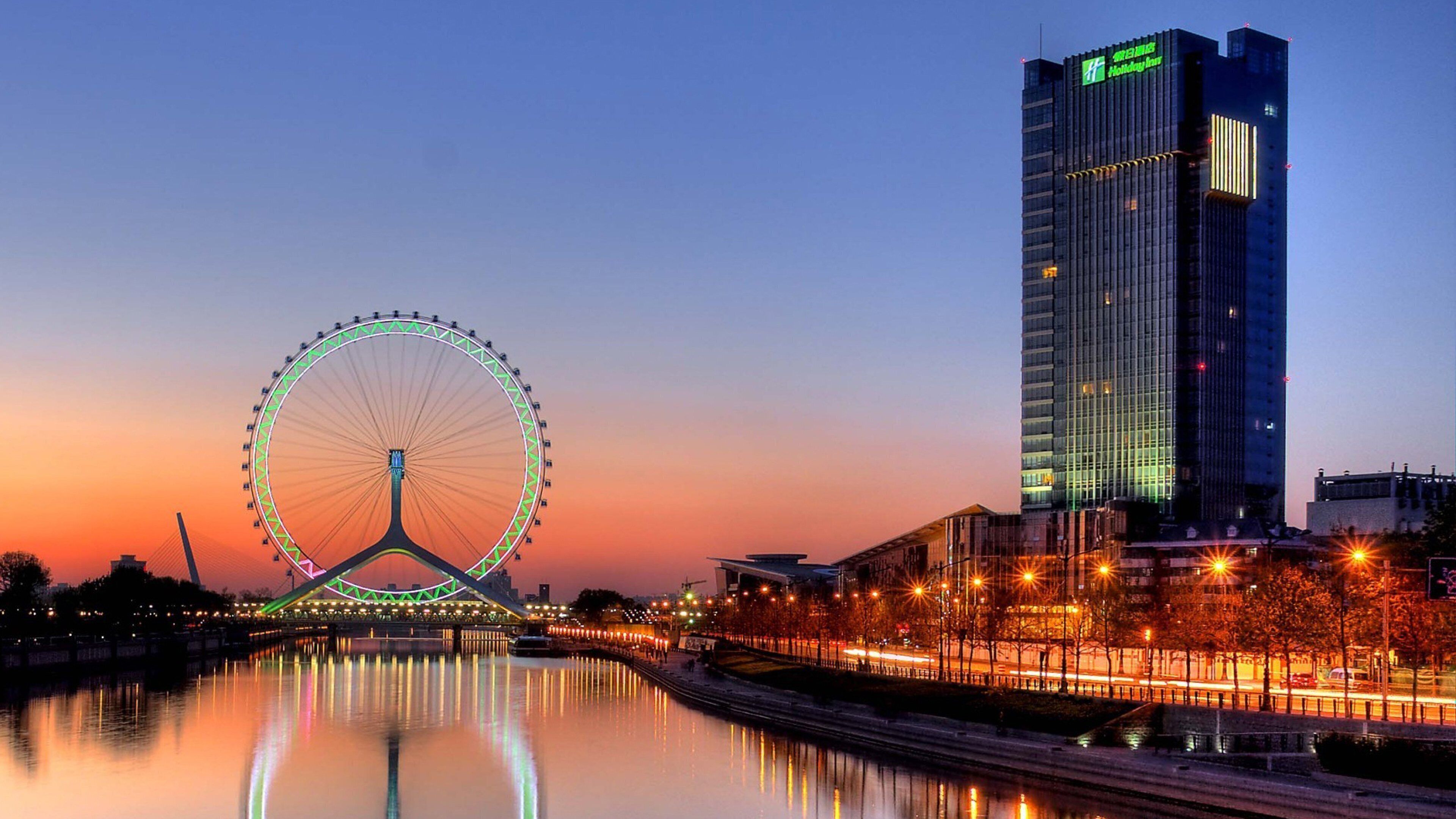 A large Ferris wheel and a tall hotel building at dusk.