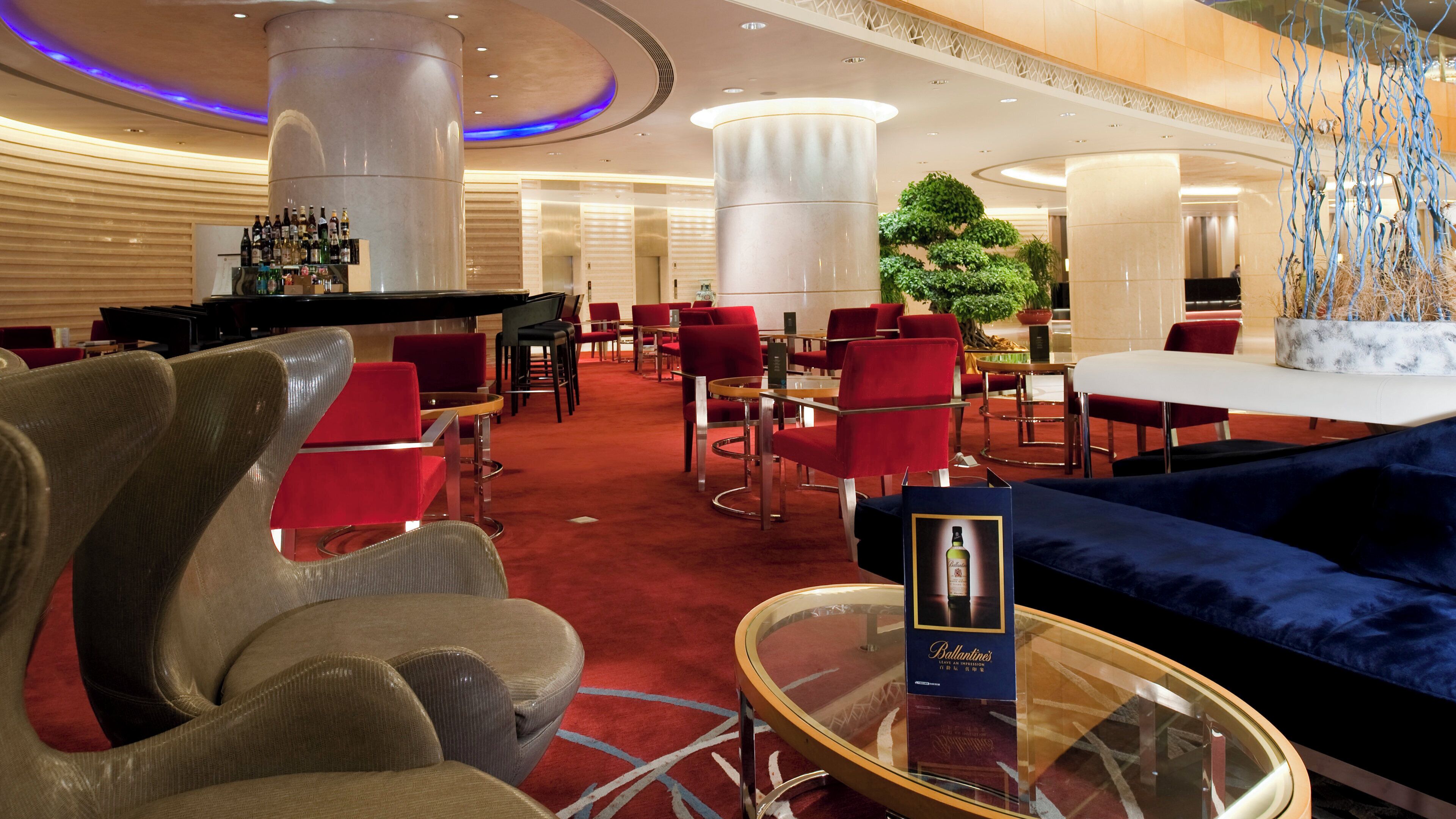A hotel lobby with red upholstered chairs, a round glass table, and a blue sofa.