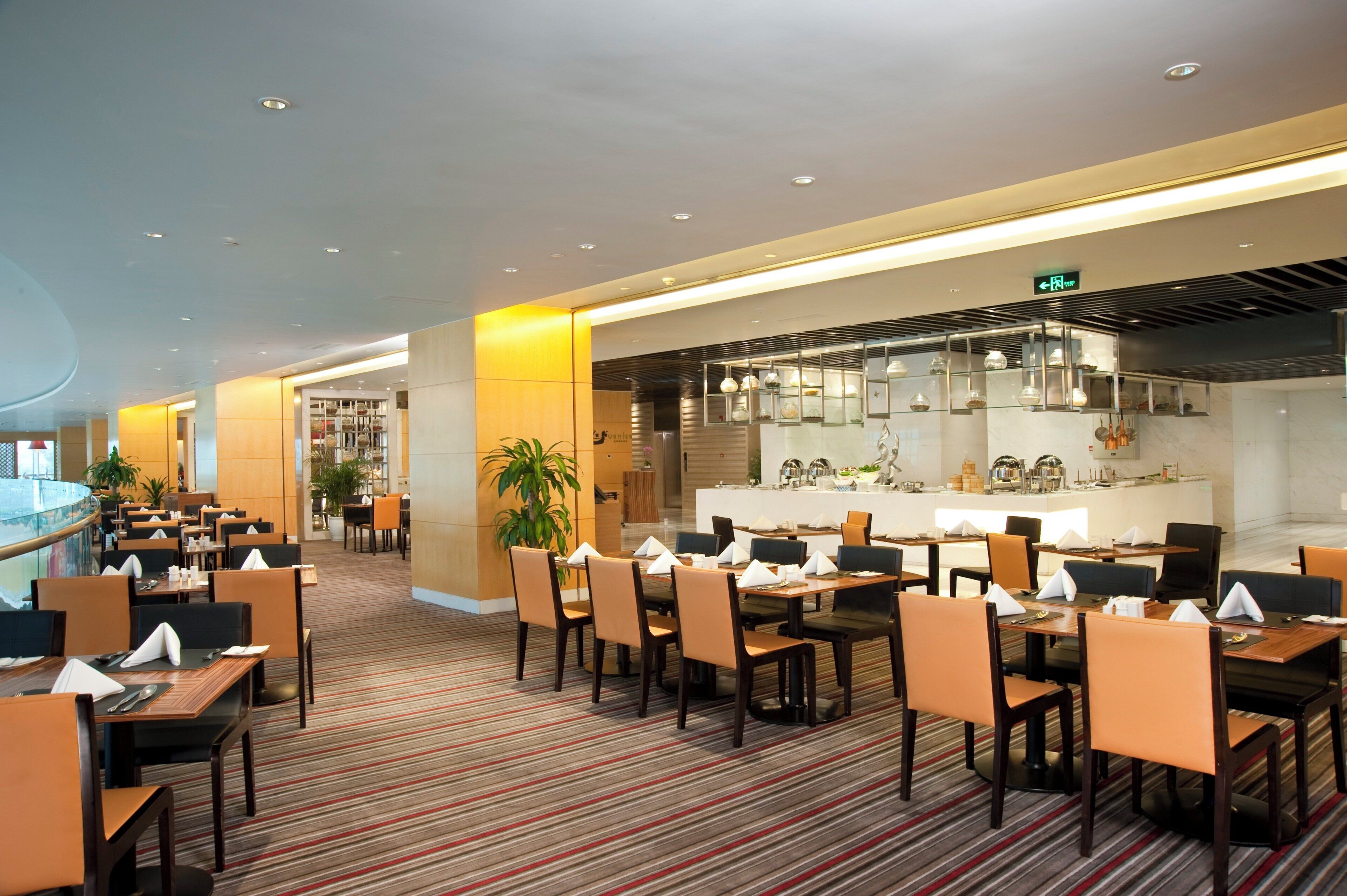 A hotel restaurant with multiple dining tables and chairs, a central bar area, and a striped carpeted floor.