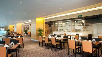 A hotel restaurant with multiple dining tables and chairs, a central bar area, and a striped carpeted floor.
