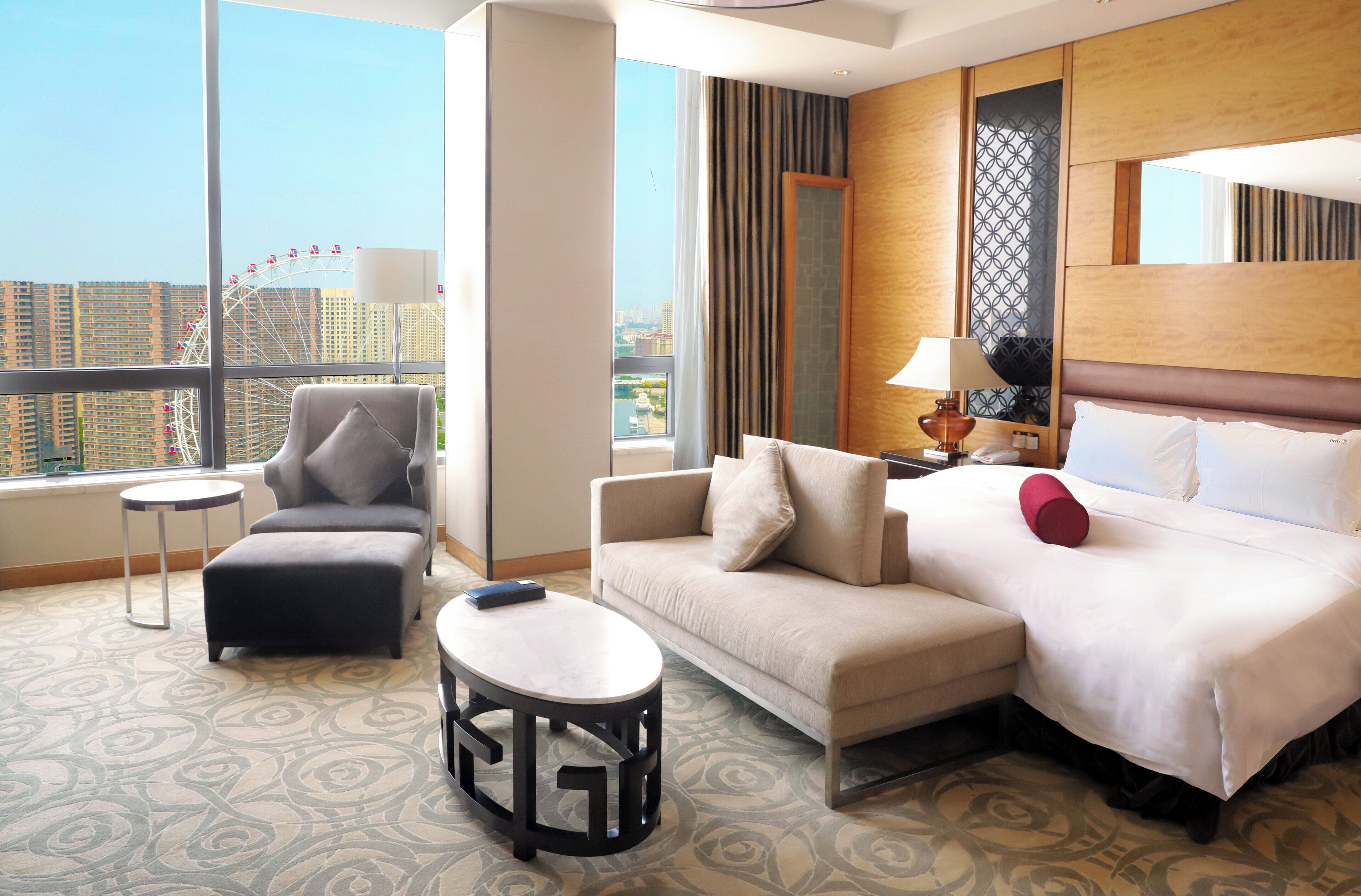 A hotel room with a large window, a sofa, a bed, a small table, and a chair.