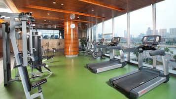 Une salle de sport équipée de matériel d’exercice, avec une grande horloge et une vue sur le paysage urbain grâce à de grandes fenêtres.