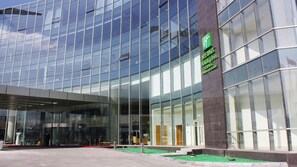 A modern building with a glass facade and a green sign indicating a Holiday Inn Express. - Holiday Inn Tianjin Riverside by IHG (Tianjin)