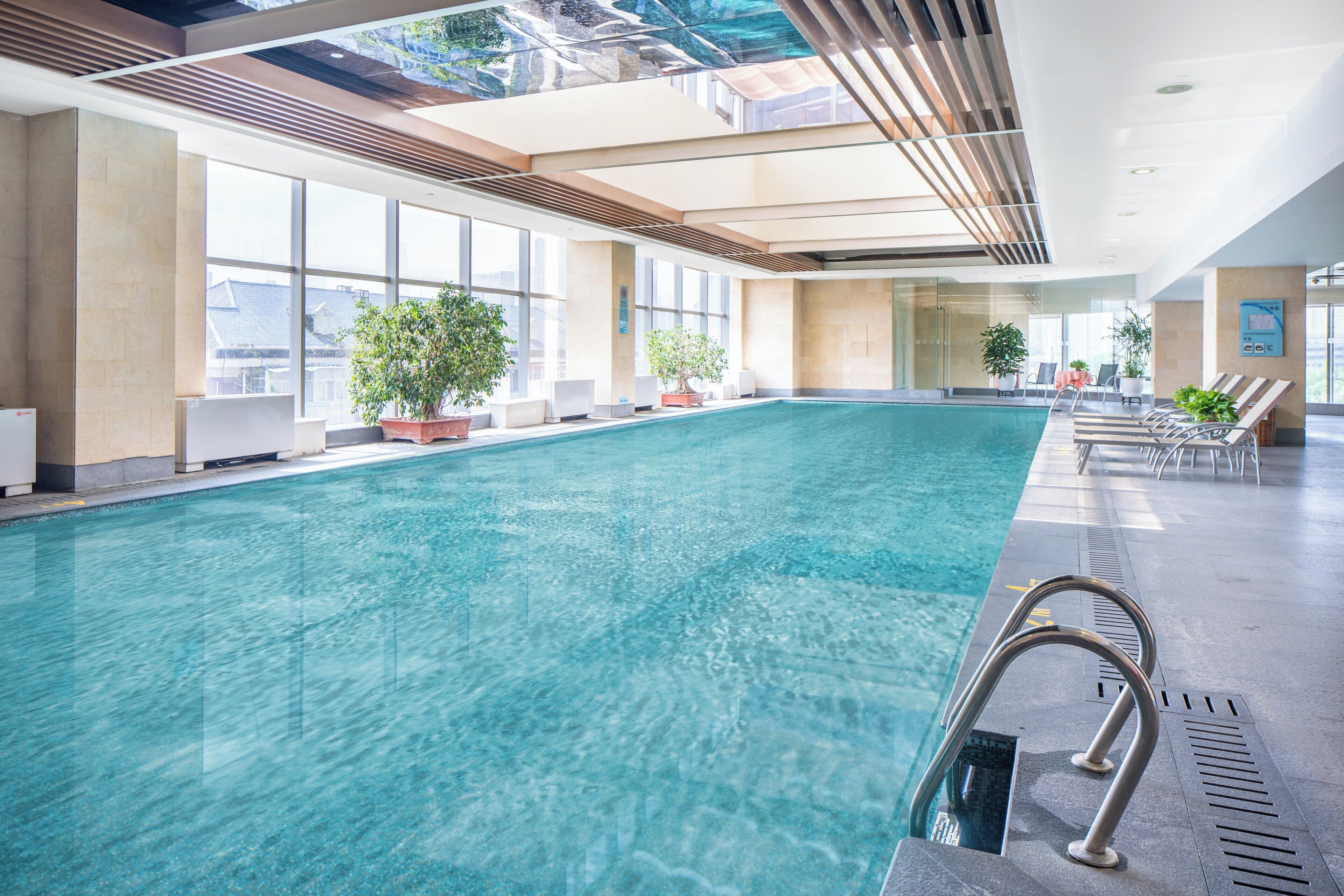 Una piscina interior con agua cristalina, rodeada de ventanas y plantas en macetas.