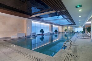 A modern indoor swimming pool with clear water, surrounded by lounge chairs and potted plants.
