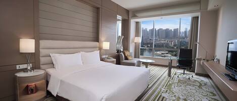 Habitación de hotel con una cama grande, un escritorio, una silla, un televisor y vistas a un paisaje urbano.