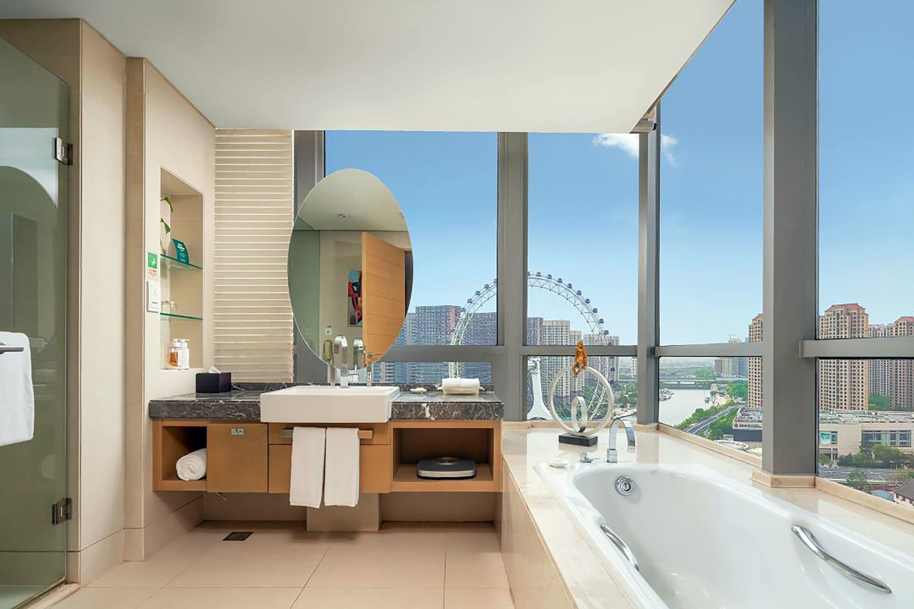 Casa de banho moderna com uma banheira grande, toucador com espelho e vista para uma roda gigante.