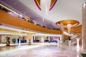Eine geräumige Lobby mit einer imposanten Treppe, mehreren Rezeptionen und einer modernen Chandelier.
