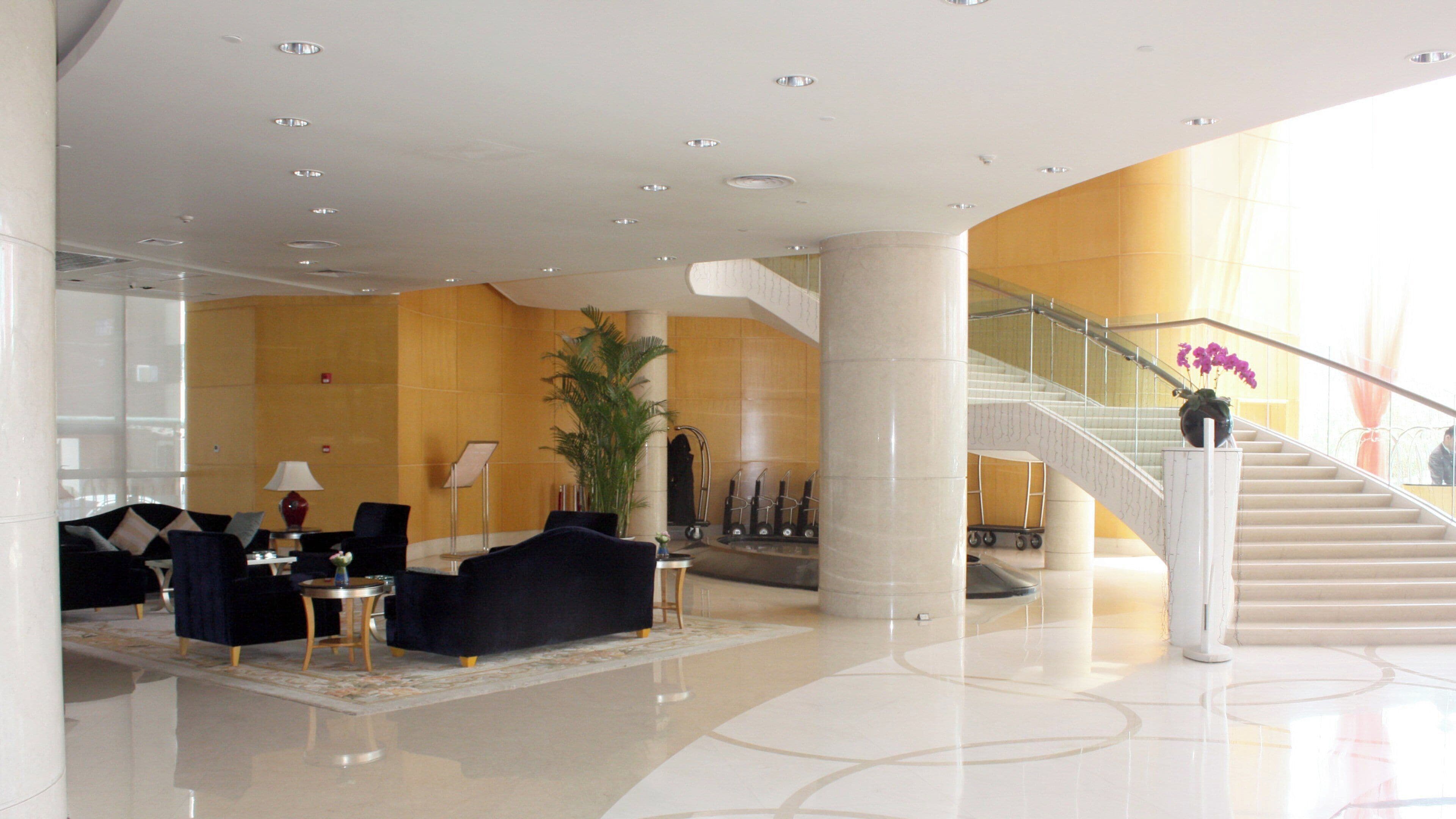 Um hall espaçoso com teto alto, escadaria e área de estar com sofás e mesas.