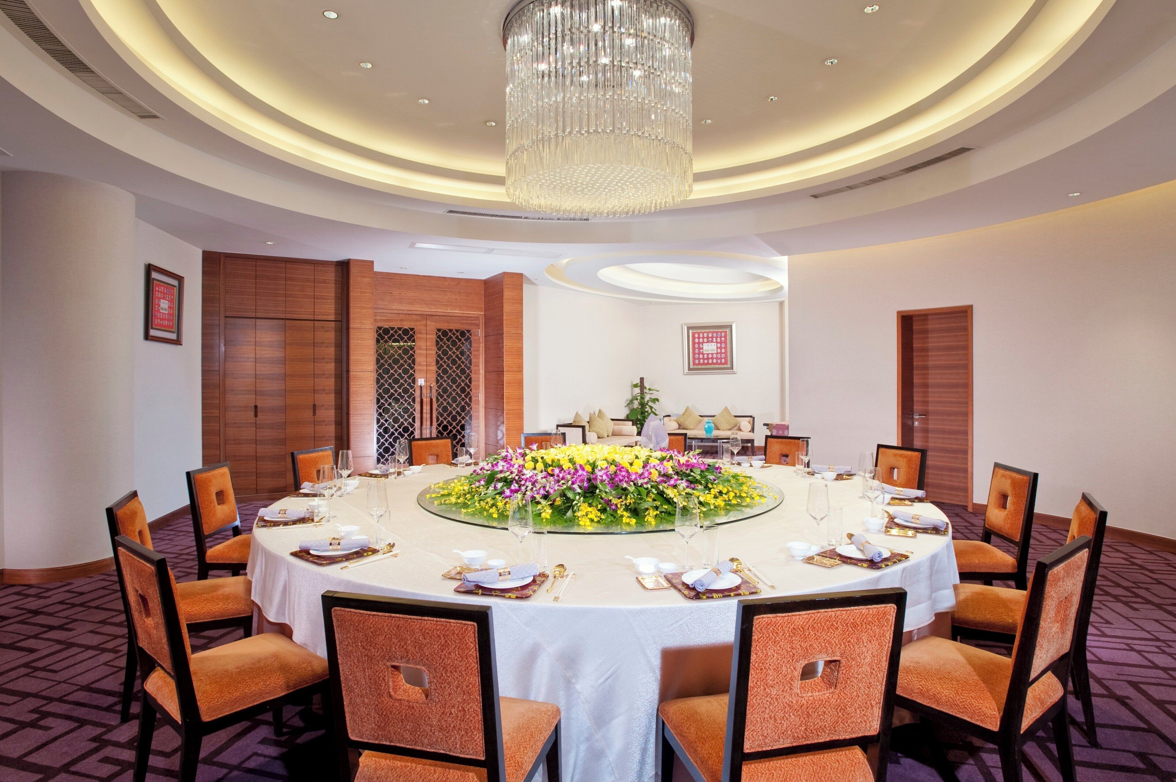 A conference room with a round table, chairs, a chandelier, and a floral centerpiece.