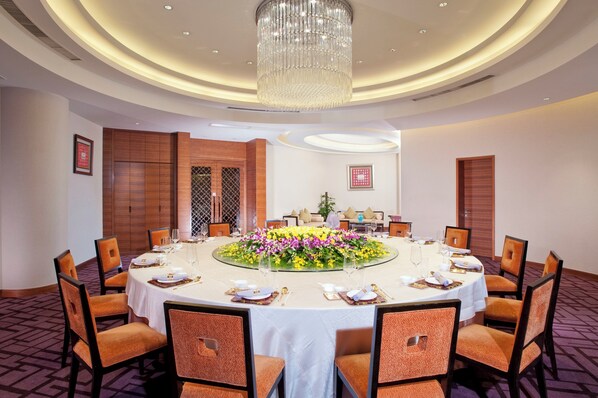 A conference room with a round table, chairs, a chandelier, and a floral centerpiece.