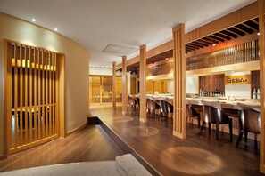 A modern interior with wooden paneling, a dining area with tables and chairs, and a bar area with bottles and glasses.