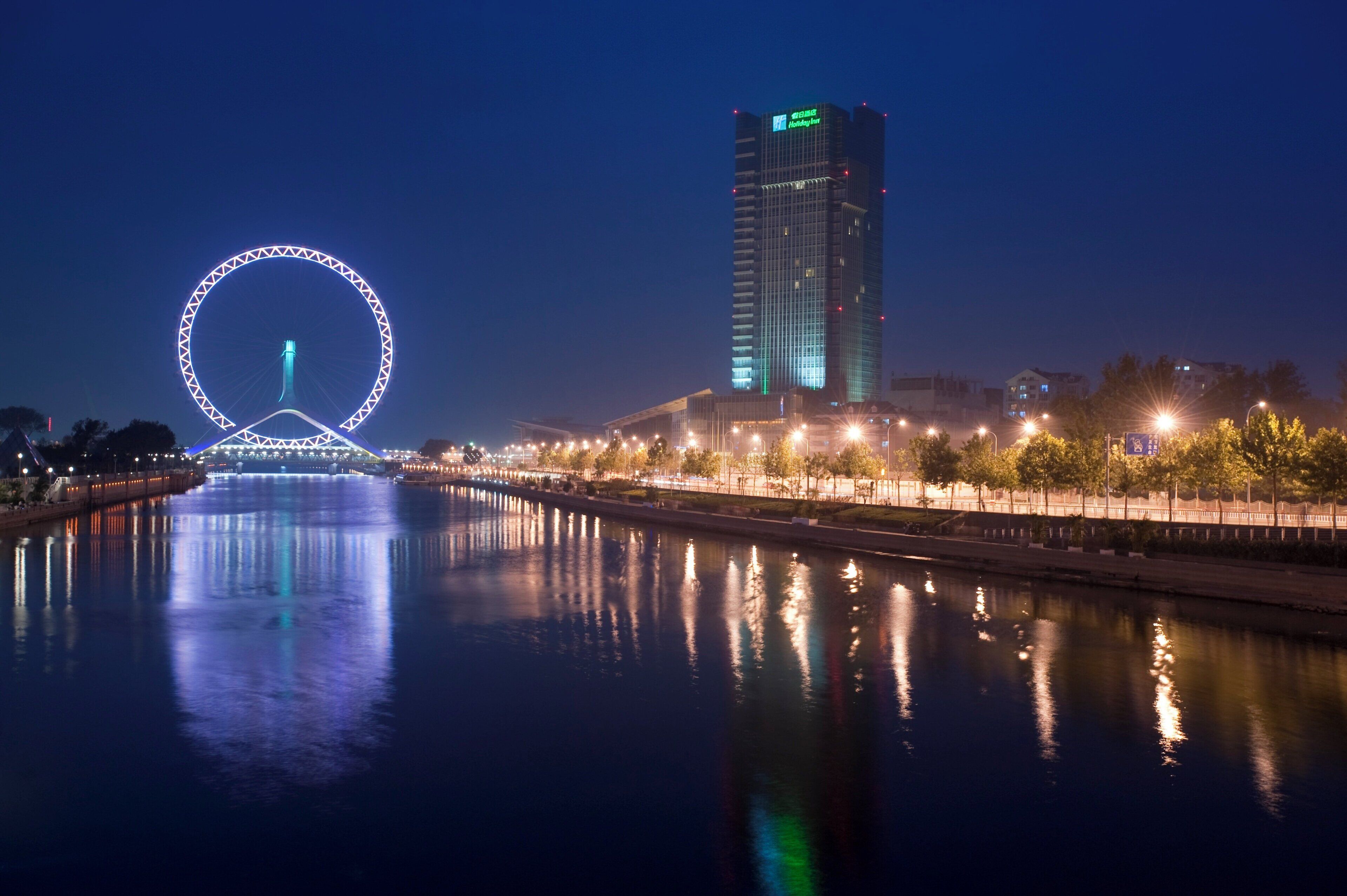 A waterfront view with a Ferris wheel and a high-rise building with illuminated signage.
