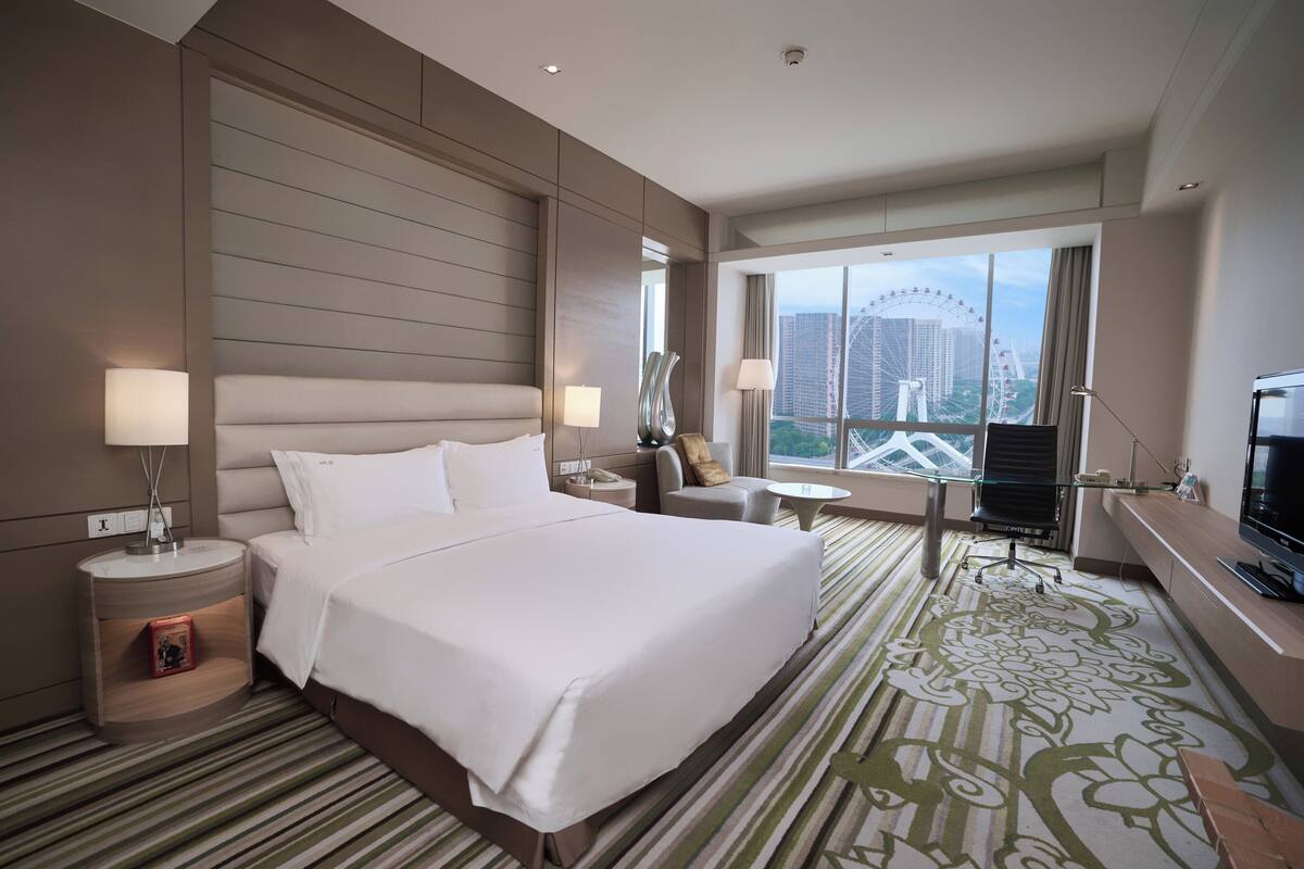 A hotel room with a large bed, bedside tables, a desk, and a view of a Ferris wheel.