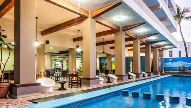 A swimming pool with lounge chairs and tables, surrounded by pillars and a ceiling with exposed beams. - Hotel Playa Bonita (Mazatlán)