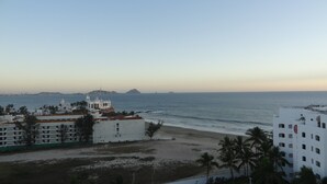 A coastal view with a beach, a white building with a bell tower, and a distant island. - Hotel Playa Bonita (Mazatlán)