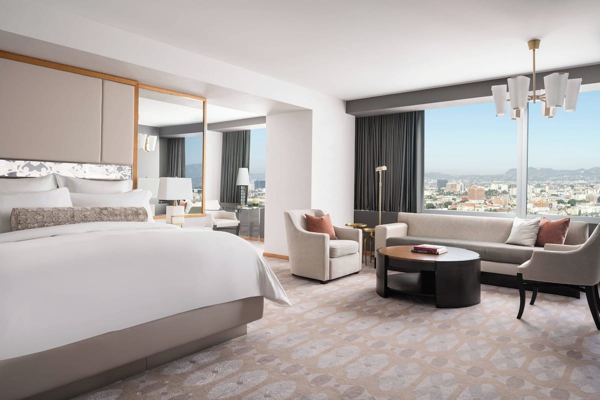 A modern hotel room with a large bed, a sofa, a coffee table, and a view of the city.