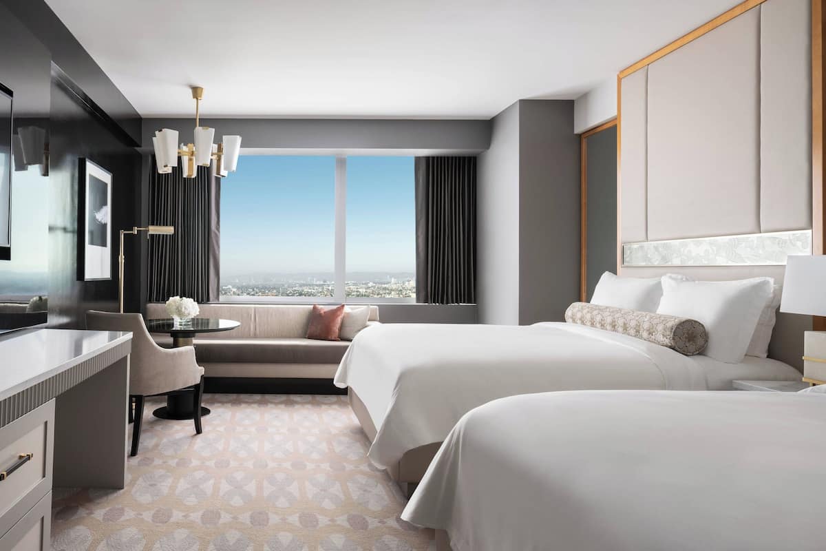 A modern hotel room with a large bed, a desk, a sofa, and a view of the city.