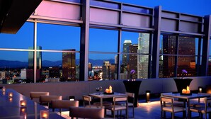 A rooftop bar with tables and chairs, large windows offering a city view, and candles on the tables. - The Ritz-Carlton, Los Angeles (Los Angeles)