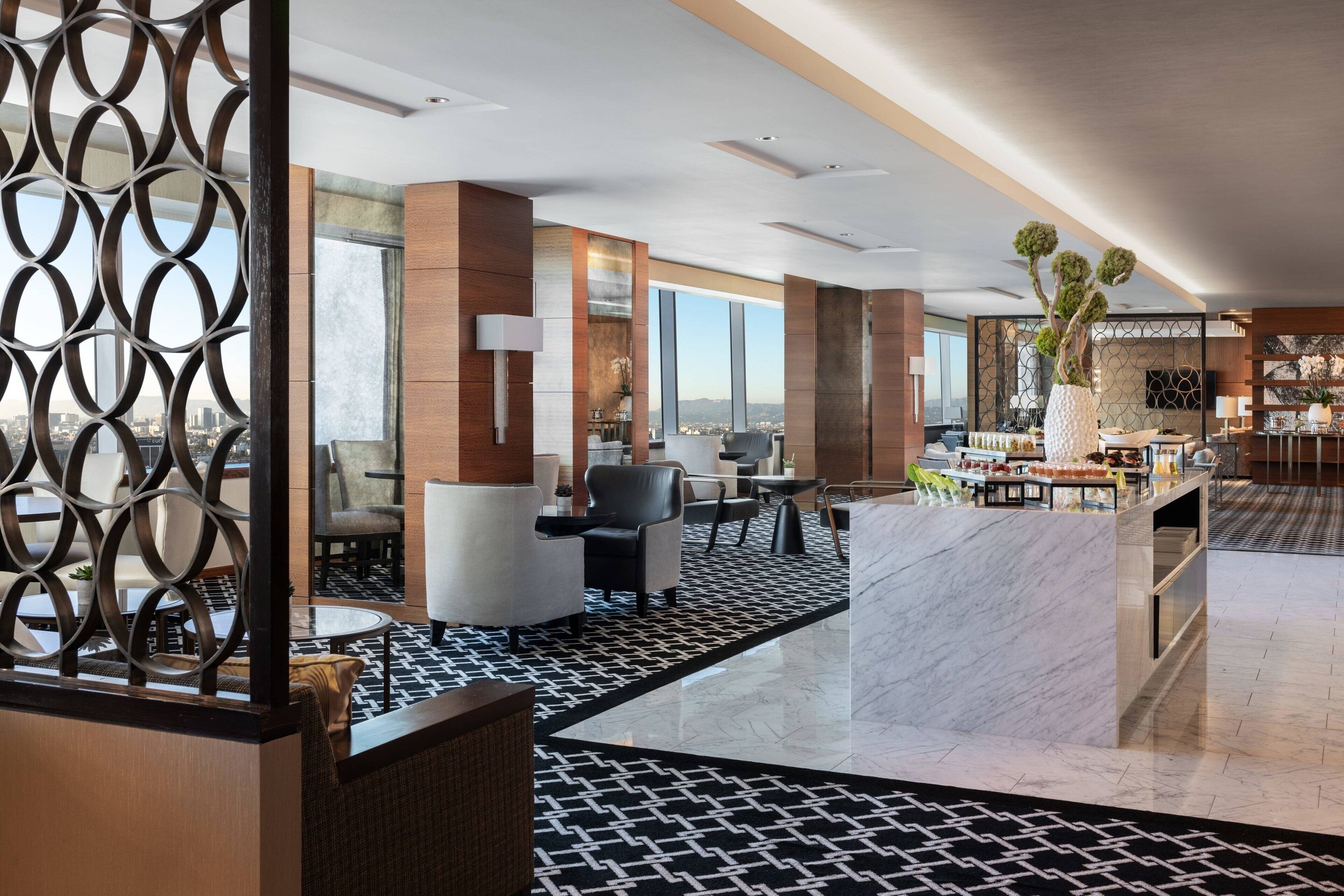 En modern hotellobby med högt i tak, en receptionsdisk, en sittgrupp och stora fönster med utsikt över staden.