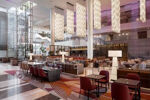 A spacious lobby with a modern design, featuring a central seating area with sofas and chairs, a bar area, and a staircase leading to upper floors. - The Ritz-Carlton, Los Angeles (Los Angeles)