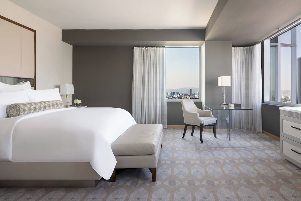 A modern hotel room with a large bed, a desk, a chair, and a view of the city.