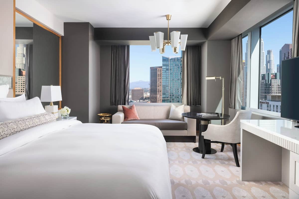 A modern hotel room with a large bed, a desk, and a view of the cityscape.