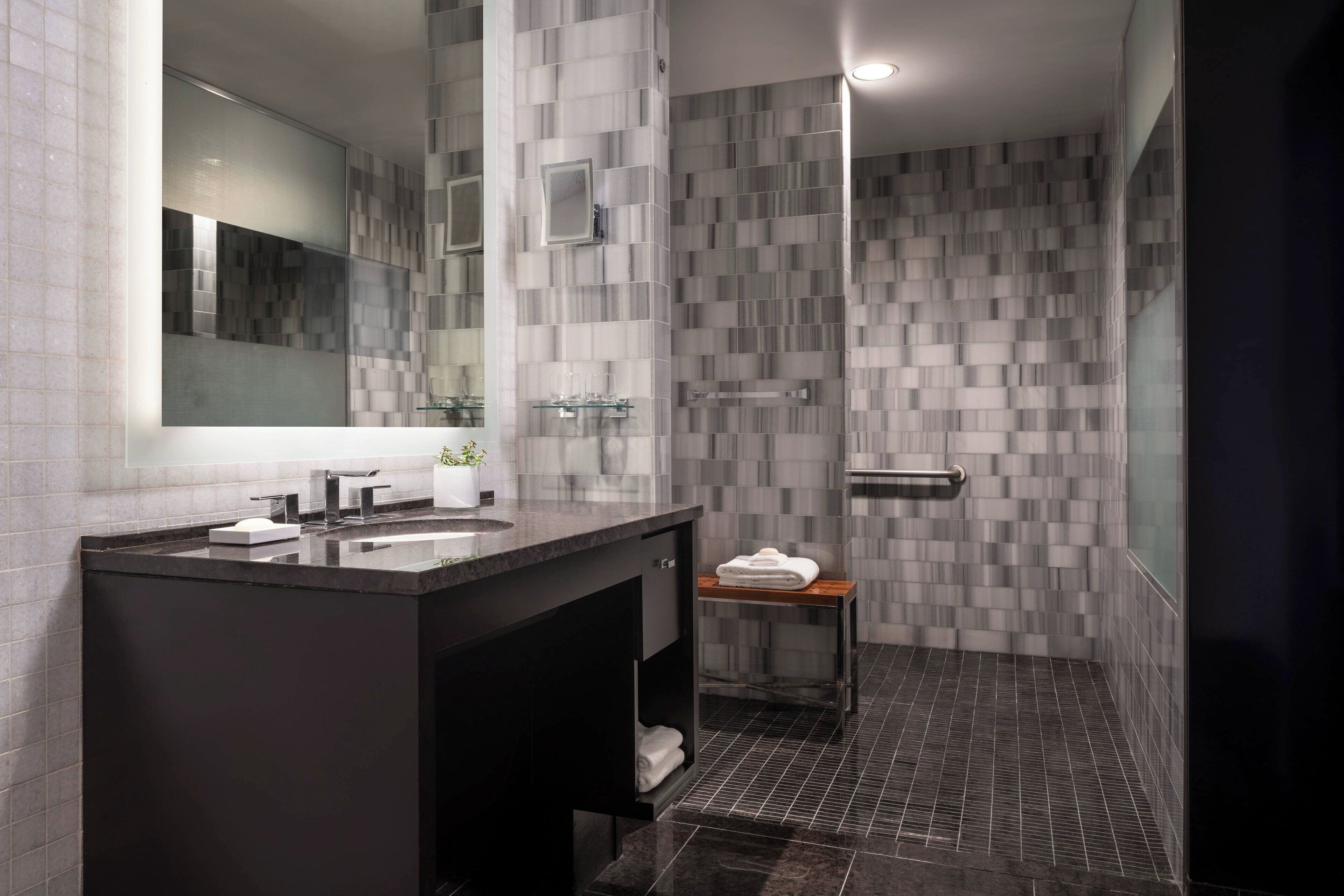 A modern bathroom with a dark vanity, a mirror, and a shower area with patterned tiles.