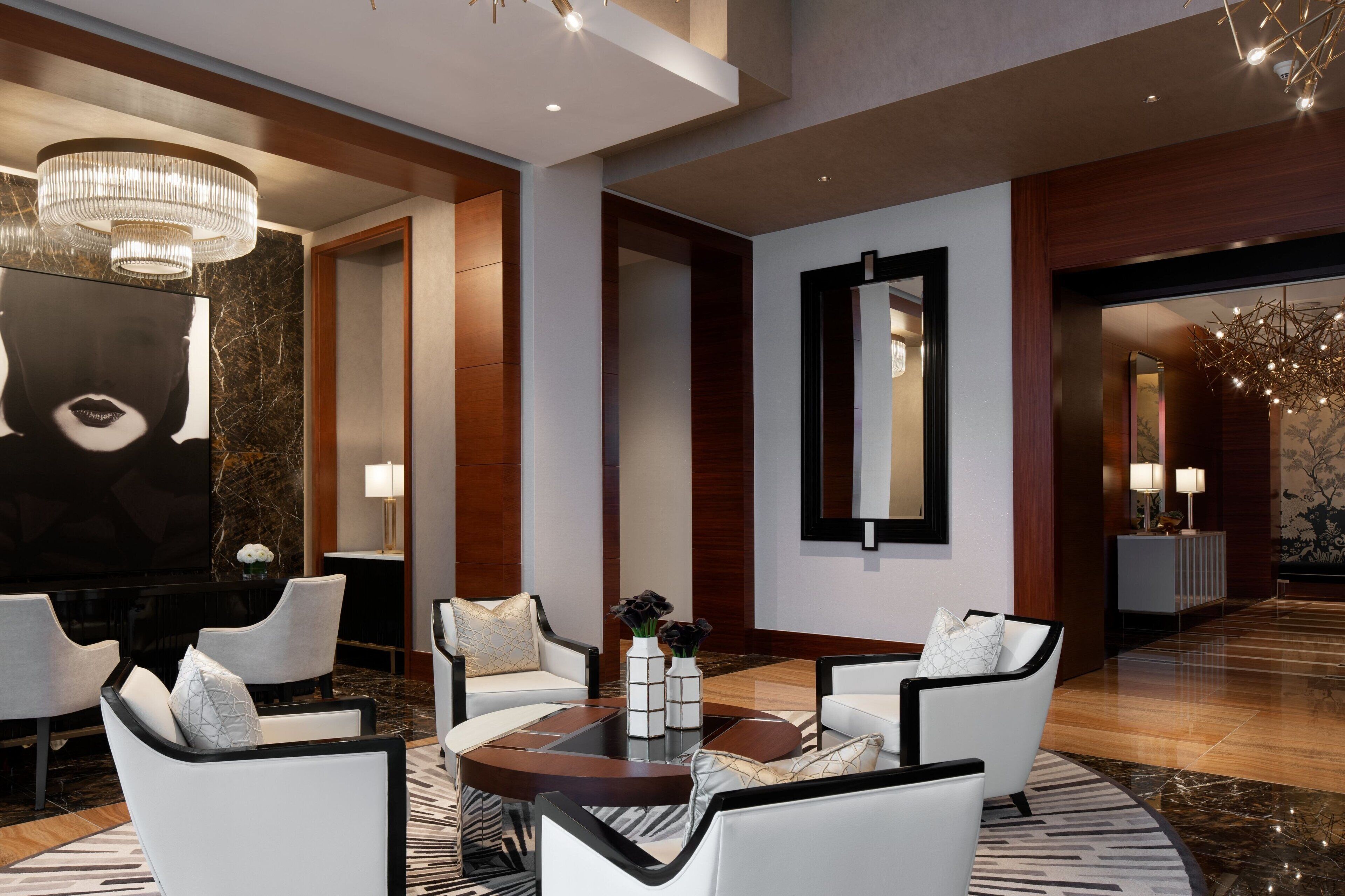 A modern lobby with a round coffee table, white armchairs, and a large mirror.