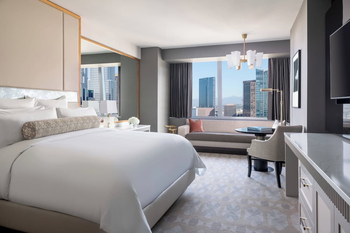 A modern hotel room with a large bed, a desk, a chair, and a view of the cityscape.