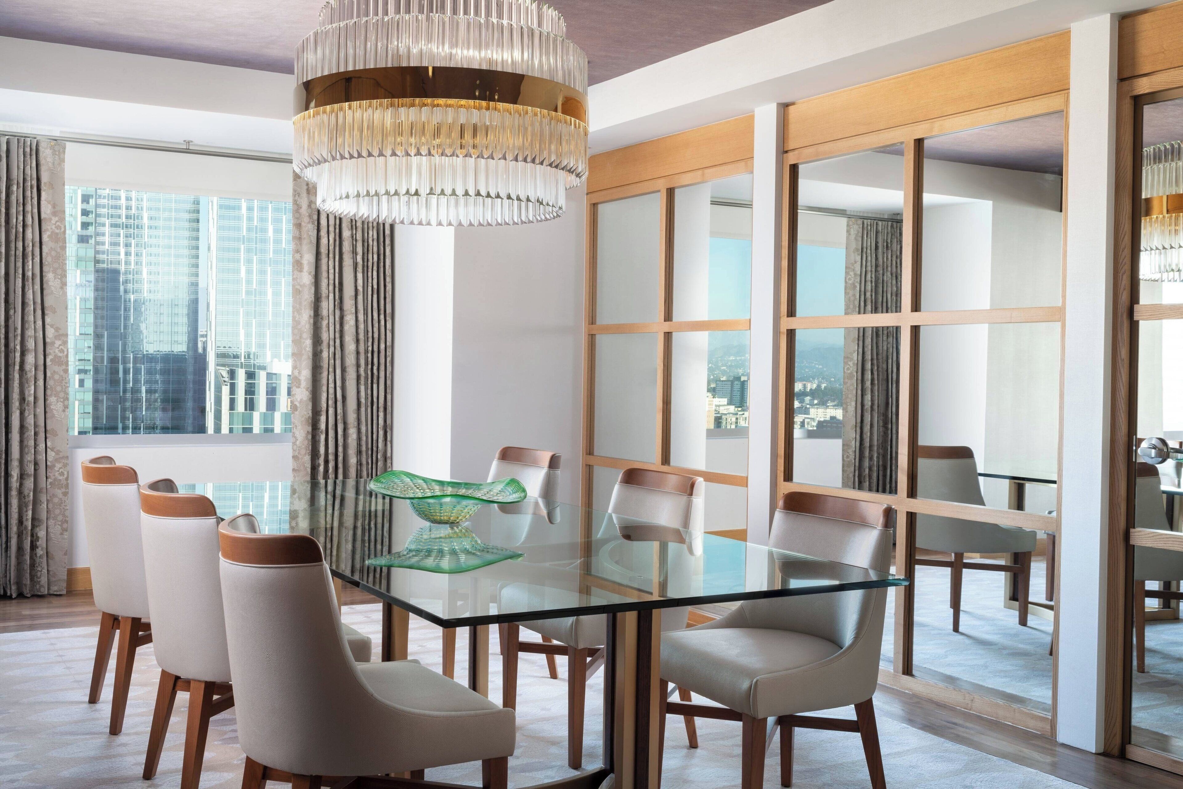 A modern dining area with a glass table, white chairs, and a large chandelier.