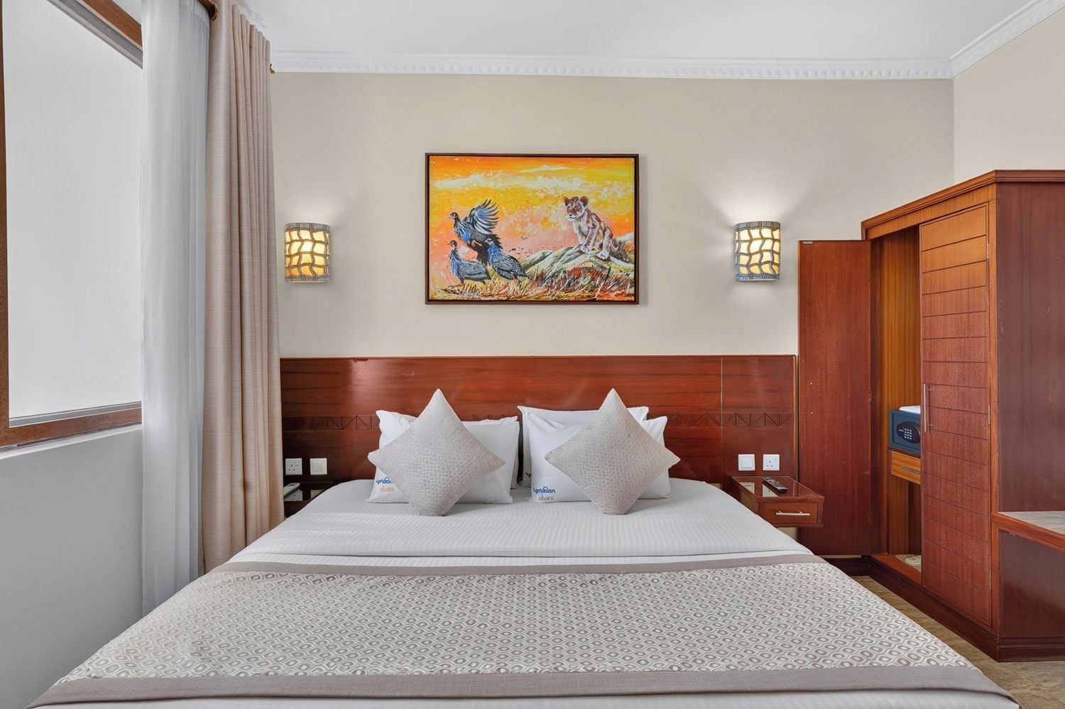 Una habitación de hotel con una cama grande, dos lámparas de noche, un cuadro en la pared y un armario de madera.