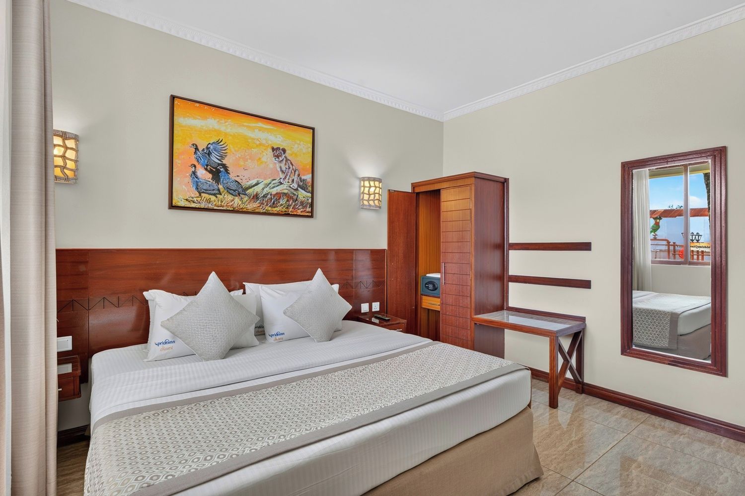 A hotel room with a large bed, a wooden headboard, a painting, a mirror, and a wooden wardrobe.
