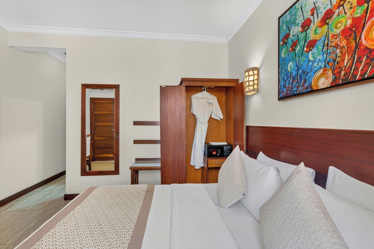 Habitación de hotel con cama, armario de madera, bata, mesita de noche y un cuadro de colores en la pared.