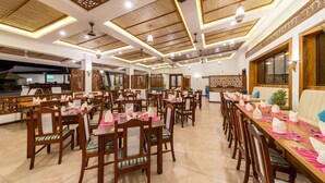 A spacious dining area with wooden tables and chairs, decorative ceiling panels, and ambient lighting. - PrideInn Hotel Diani (Diani Beach)